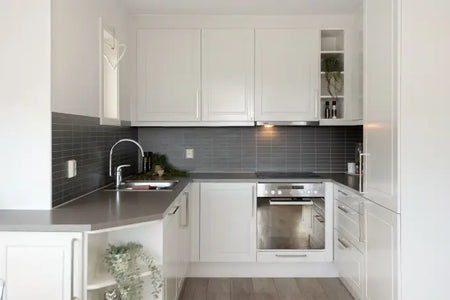 White L-shaped kitchen with gray countertop, backsplash, sink, and built-in oven.